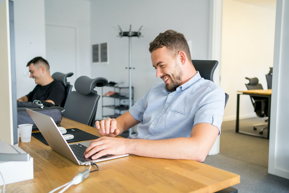 Smiling man working on a laptop in a modern office, with a colleague in the background