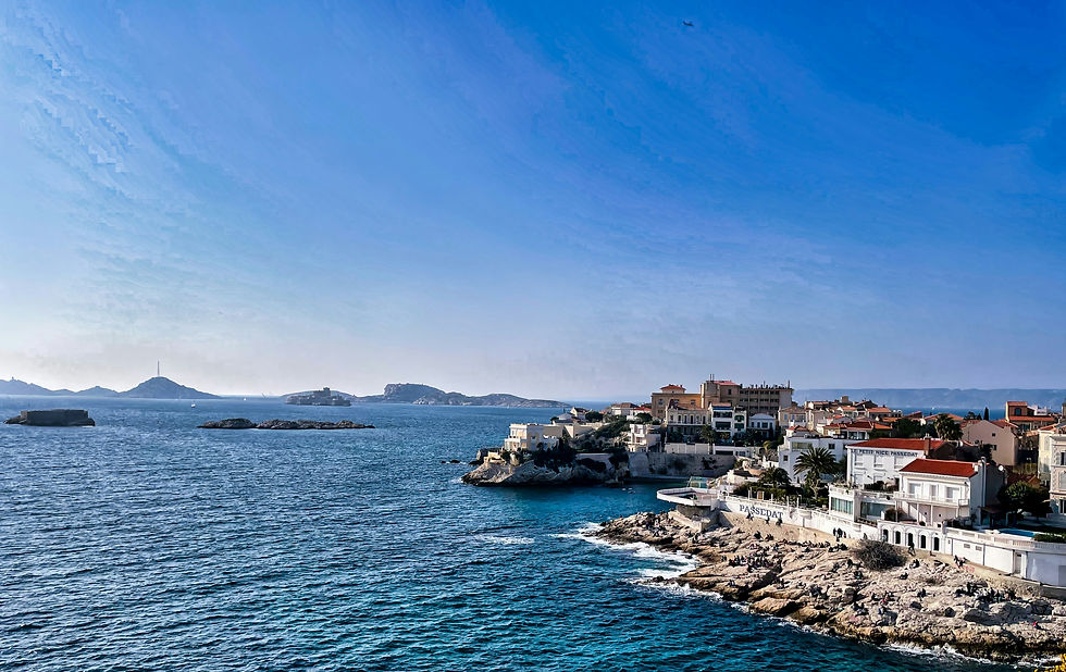 A serene Provençal coastal town built along rocky cliffs with pastel buildings and red‑tiled roofs overlooking calm blue water.