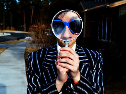 a person in a pinstripe suit and blue sunglasses looking through a large magnifying glass