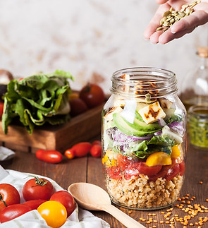 Healthy salad in a jar being prepared with tomatoes, lettuce, red onion, avovado, cheese and sunflower seeds