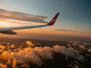An airplane wing glides above a golden-hued cloudscape at sunset, capturing the serene beauty of skyward travel.