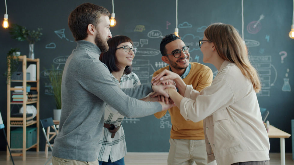 Team clasping hands in middle of office in celebration of work accomplished.
