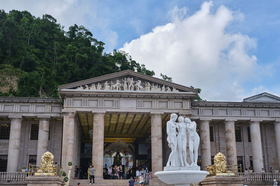 Neoclassical building with columns, statues, and gold lion sculptures. People gather outside under a blue sky with fluffy clouds.