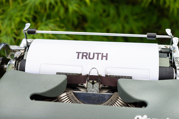 Close-up of a vintage typewriter typing "TRUTH" on white paper. Green foliage background adds a natural contrast.