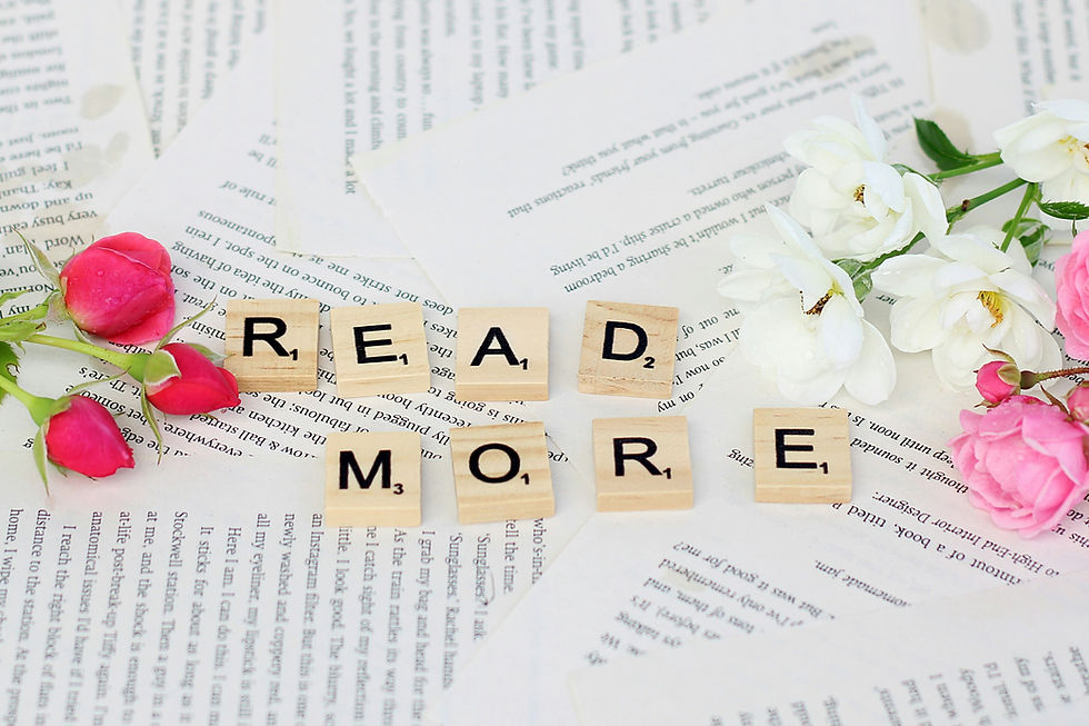 Scrabble tiles spelling "READ MORE" amid open book pages, surrounded by pink and white flowers