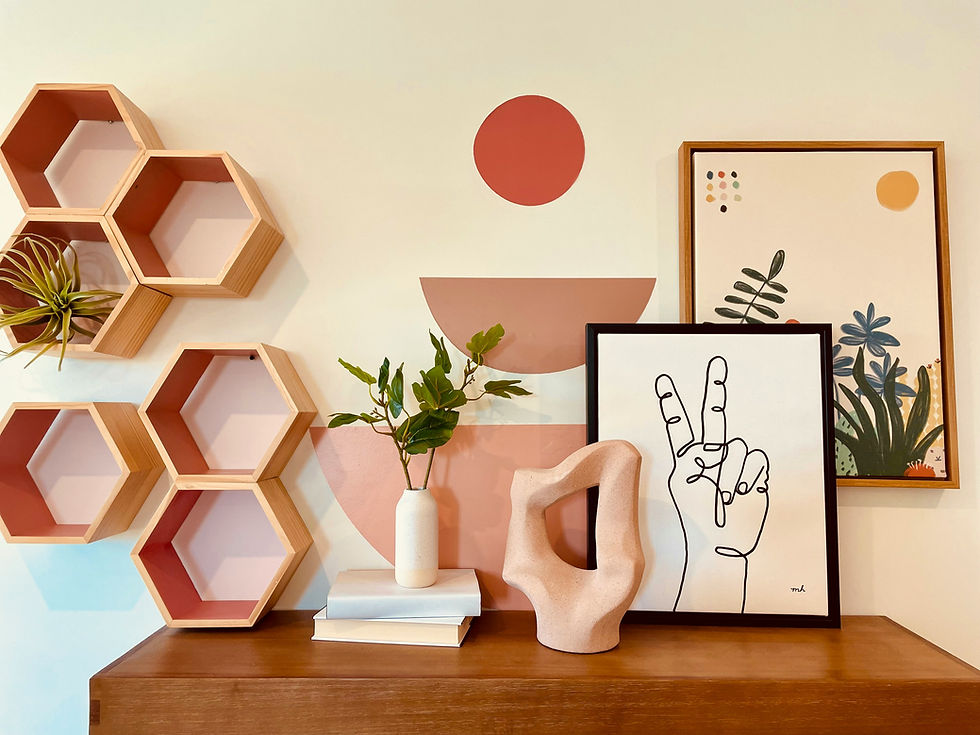 Decorative shelf with hexagon wall shelves, framed abstract art, potted plant, vase, and pink sculptural object on a wooden table.