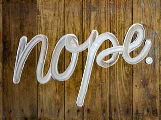 The word "nope" is painted in grayish-white paint on a brown wooden fence.