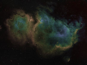 A nebula shines with colors of green, yellow, red, and blue against a dark and starry backdrop of outer space.