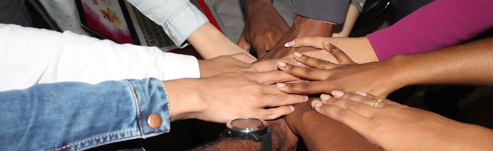 A diverse group of volunteers stands together, their arms and hands forming a circle. They represent various LGBTQ+ identities and ethnic backgrounds, including Black, Brown, Latinx, White, Asian, Pacific Islander, Indian, and Native American. Together, they are joyfully celebrating a significant event dedicated to volunteering.