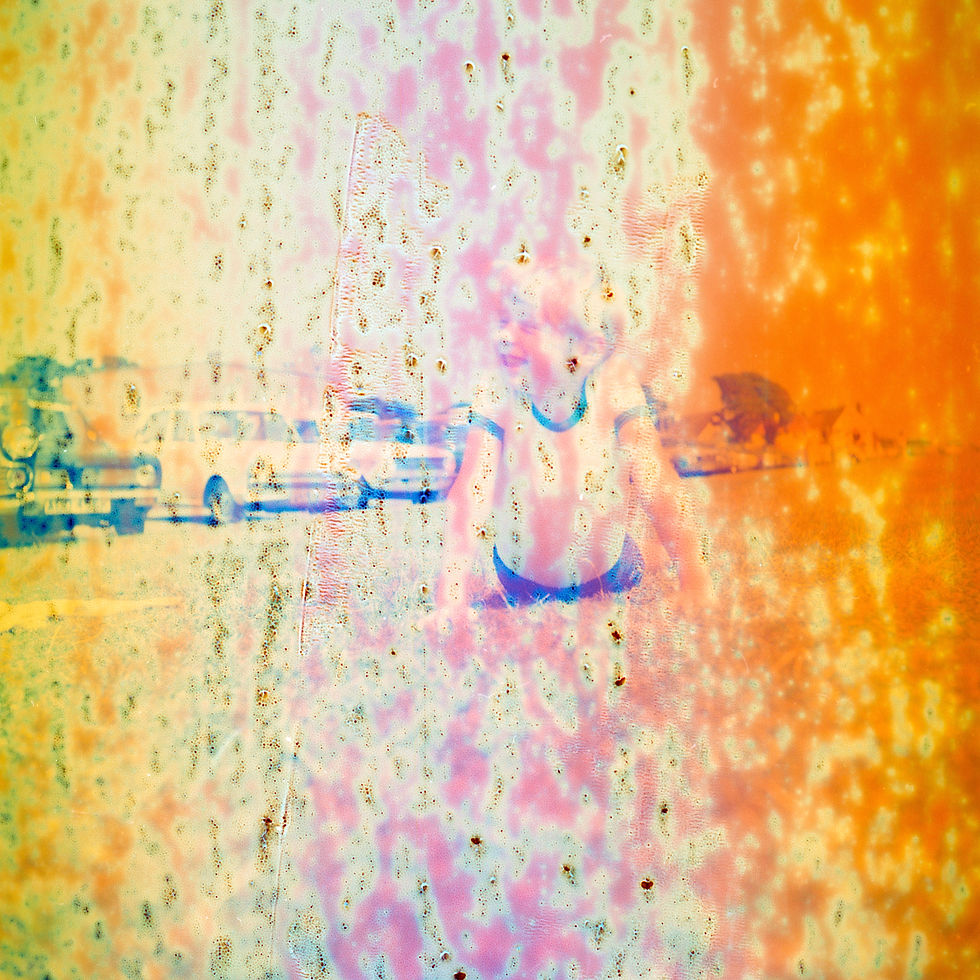A person on a beach, blurred by colorful patterns and textures. Vintage cars in the background, orange and pink hues dominate the scene.