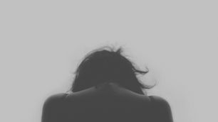 Silhouette of a person with head down, hair slightly disheveled, set against a plain gray background, evoking a somber mood.