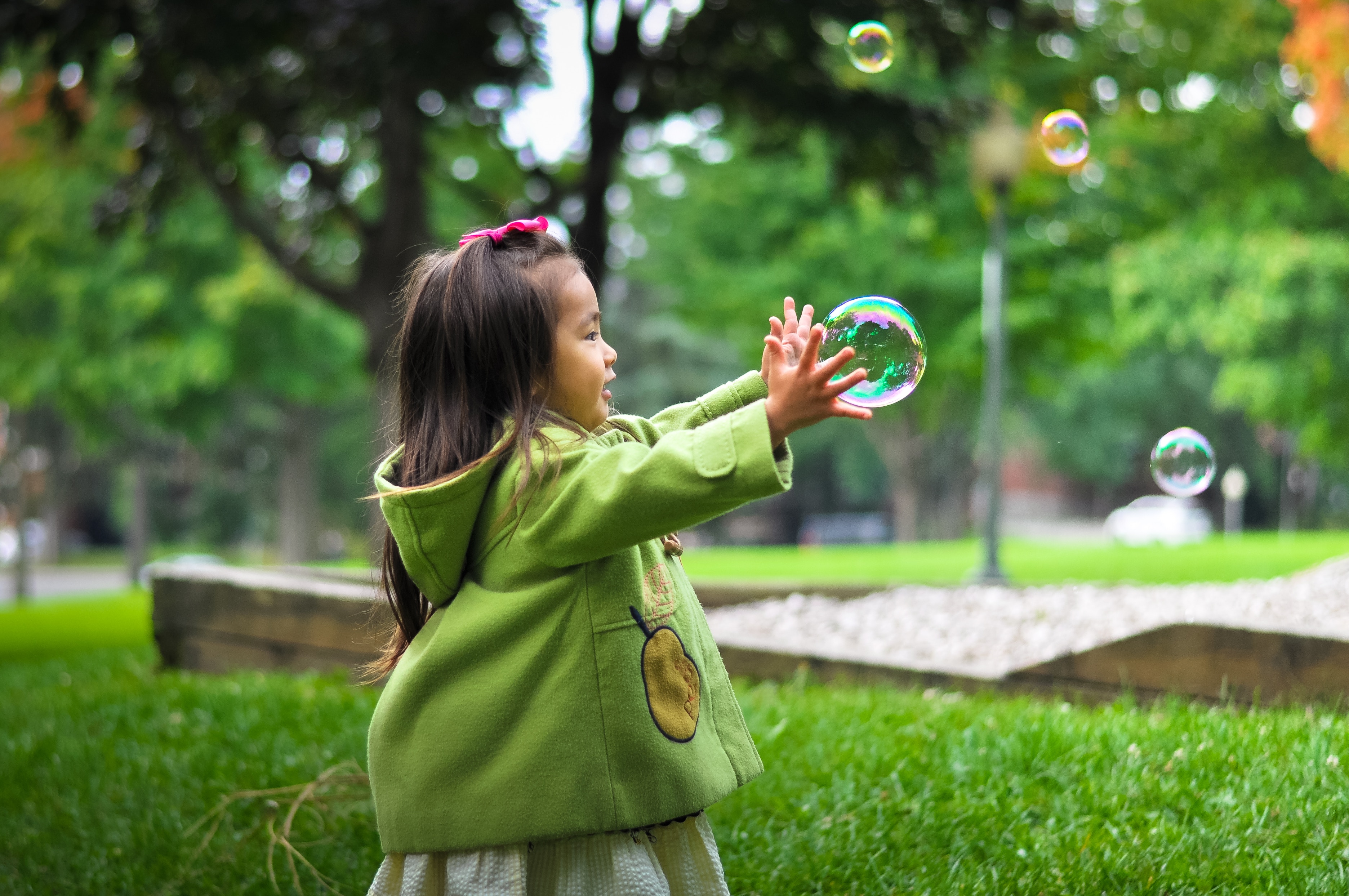 Young child reaches toward bubbles outdoors