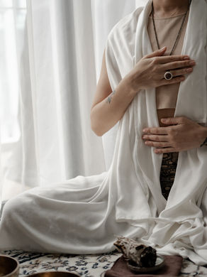 Frau in weissem Gewand beim Meditieren. Man sieht den Kopf nicht aber eine Hand auf dem Herz, eine auf dem Bauch.