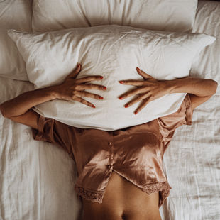 Woman lying in satin pajamas on bed, representing sleepless nights and bedtime anxiety