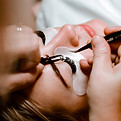 A woman receiving lash extensions, with a technician carefully applying them to her natural lashes