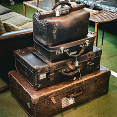 A stack of four vintage leather suitcases with luggage tags sits on a green carpet