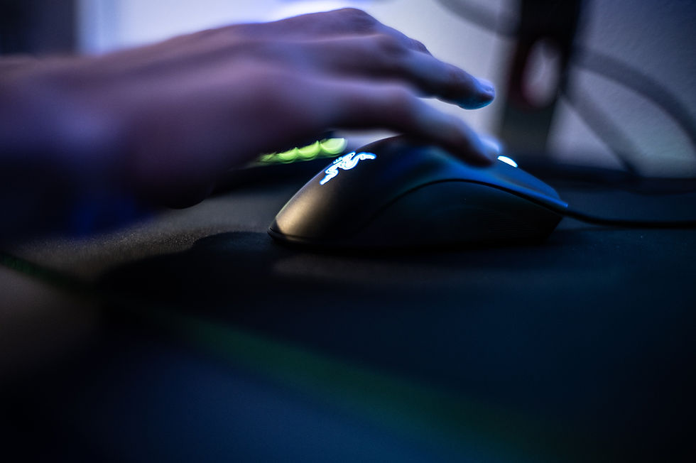 A hand using a mouse on a black mat beside a laptop, with a design on the nails. The person wears a blue shirt.