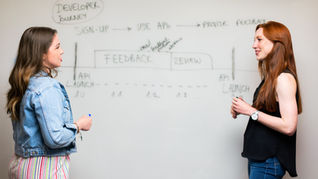 Zwei Frauen die sich vor einem Whiteboard gegenüberstehen und zwischen ihnen steht u.a. "Feedback"
