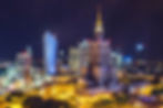 Warschauer Skyline bei Nacht, beleuchtete Hochhäuser; zentrales Gebäude mit Turm. Lebhaftes Stadtbild, bunte Lichter, dunkler Himmel.