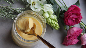 Ghee in a glass jar with a spoon and flowers around the jar, representing one of three Ayurvedic self-care products recommended for a daily self-care routine