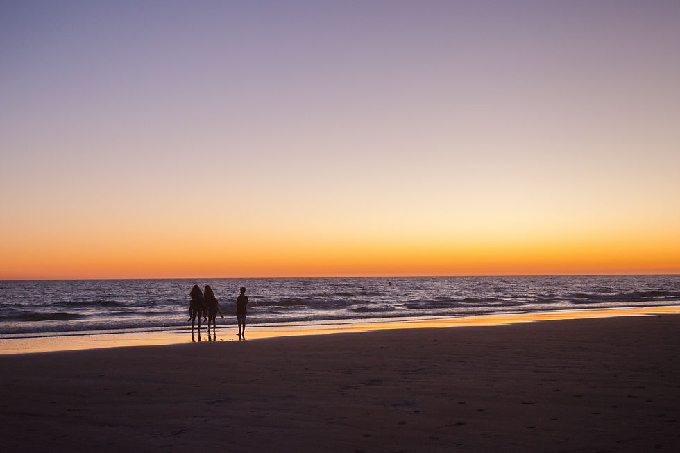 A group of people enjoy a serene walk along the beach as the sky transitions from vibrant orange to deep purple during a breathtaking sunset.