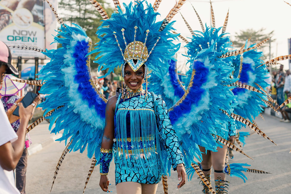 Person in vibrant blue feathered costume, smiling at a carnival parade in Aruba. Bright, intricate headdress and fringe details. 
