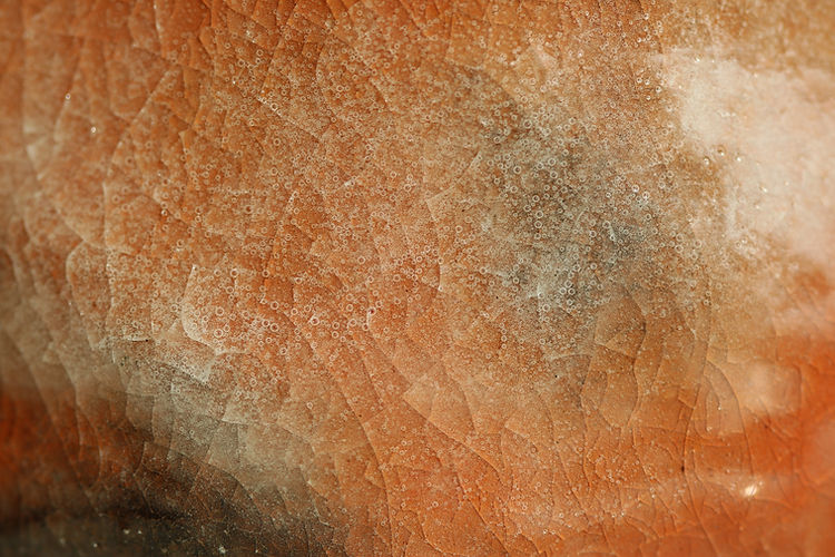 A close up image of a ceramic piece showing an orange and white crackle glaze.
