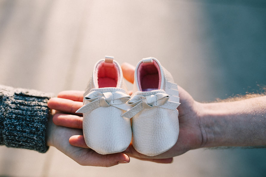 woman holding white baby shoes