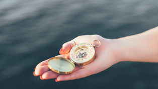 Person's hand holding a compass over water