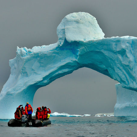 Gommone zodiac con gente a bordo naviga vicino ad un grande iceberg che forma un arco sul mare