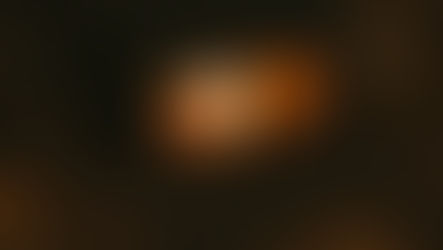 A woodburning fireplace in a dark room with orange flames burning inside it and piles of chopped wood stacked all around.