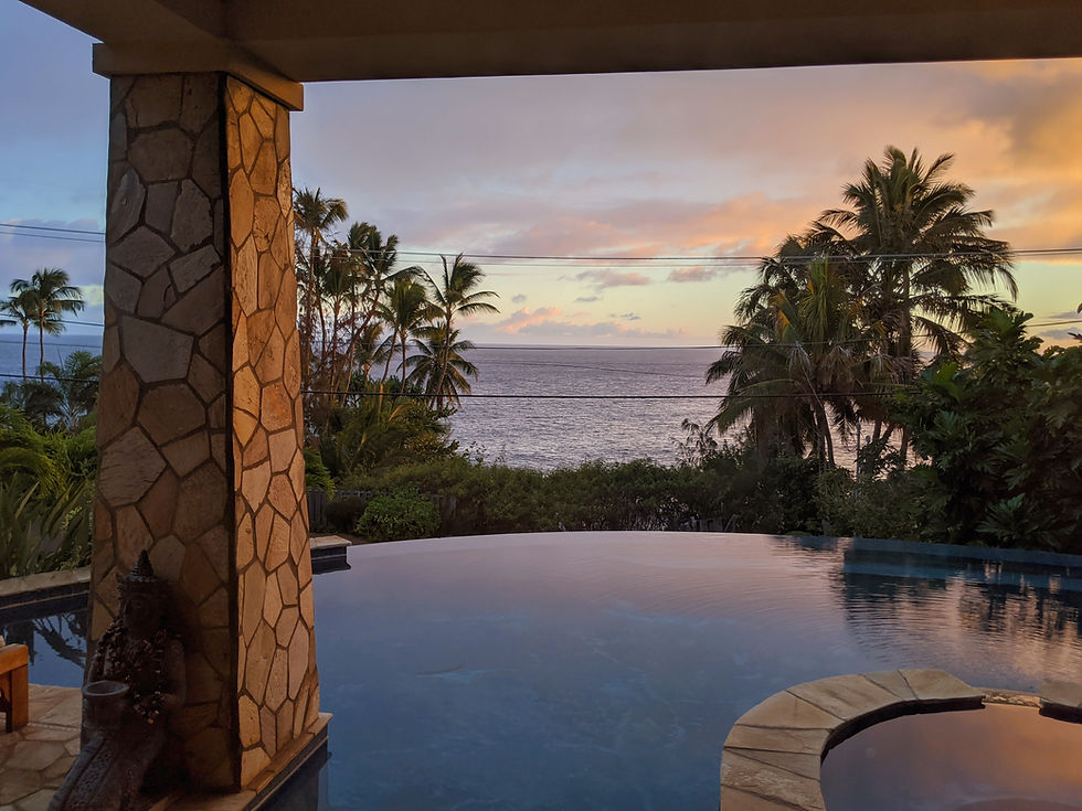 Tropical sunset over ocean behind palm trees and an infinity pool, framed by a stone pillar and patio, calm and luxurious.