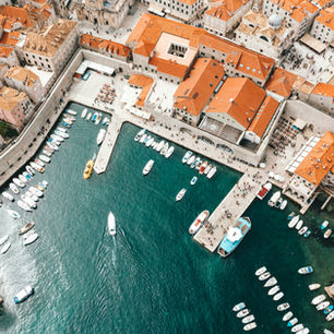 A stunning aerial view of Dubrovnik, Croatia, showcases its historic harbour with boats docked near the iconic city walls and vibrant red-tiled roofs, reflecting the charm and heritage of the medieval old town.