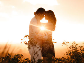 Couple embraces at sunset in a field, creating a silhouette with a warm golden glow. Romantic and serene atmosphere.