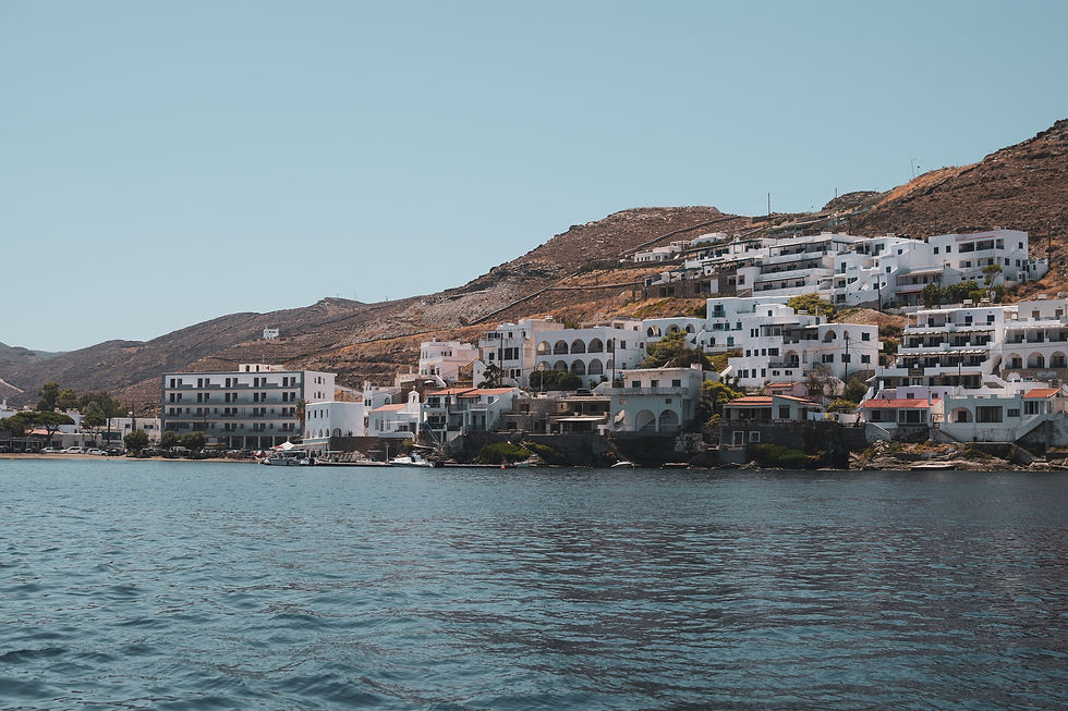 Coastal hillside with white buildings, calm sea in foreground, and clear blue sky. Peaceful and sunny Mediterranean atmosphere.
