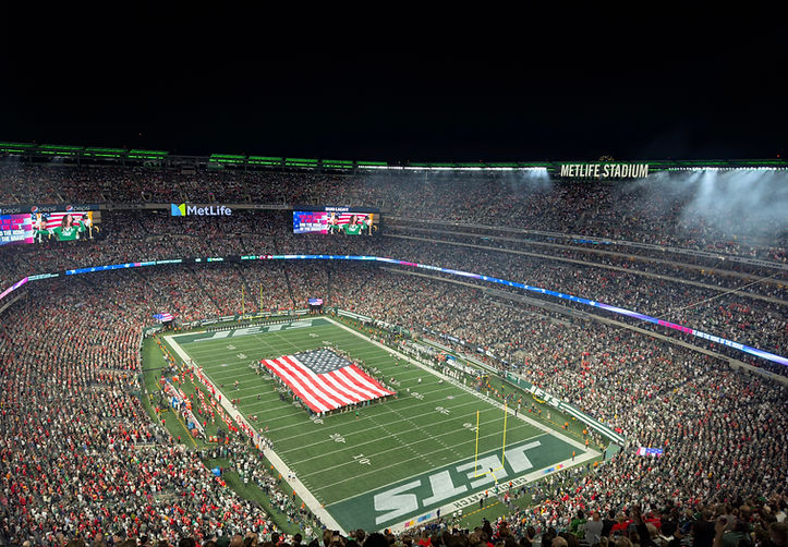 Jets football field at MetLife Stadium, packed with fans, featuring an American flag stretched across the field.