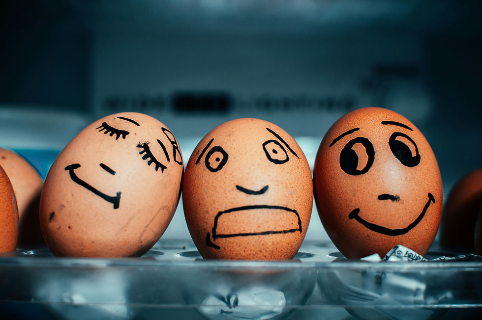 Three eggs with drawn faces show various emotions: content, worried, and happy. They sit in a fridge against a blurred background.