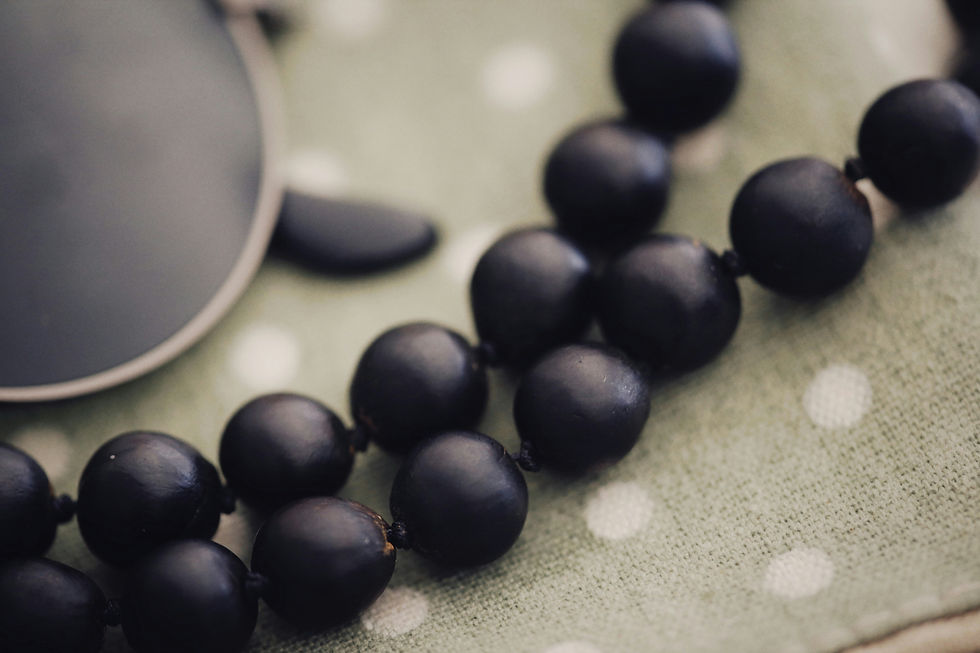 Black beads on a textured green cloth with white polka dots. A corner of a black-rimmed object is visible, creating a calm mood.