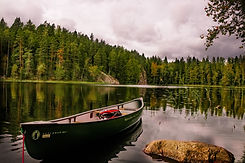 A canoe sits empty on the shores of a calm lake with forest in the background