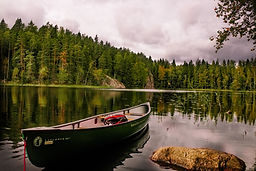 Image by SaiKrishna Saketh Yellapragada of an empty canoe floating on the ege of a lake with a hill of trees in the background.