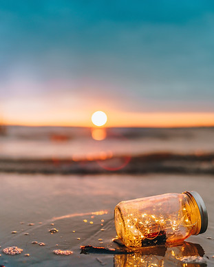 A bottle with fairy lights on the beach with the Portuguese sunset as background