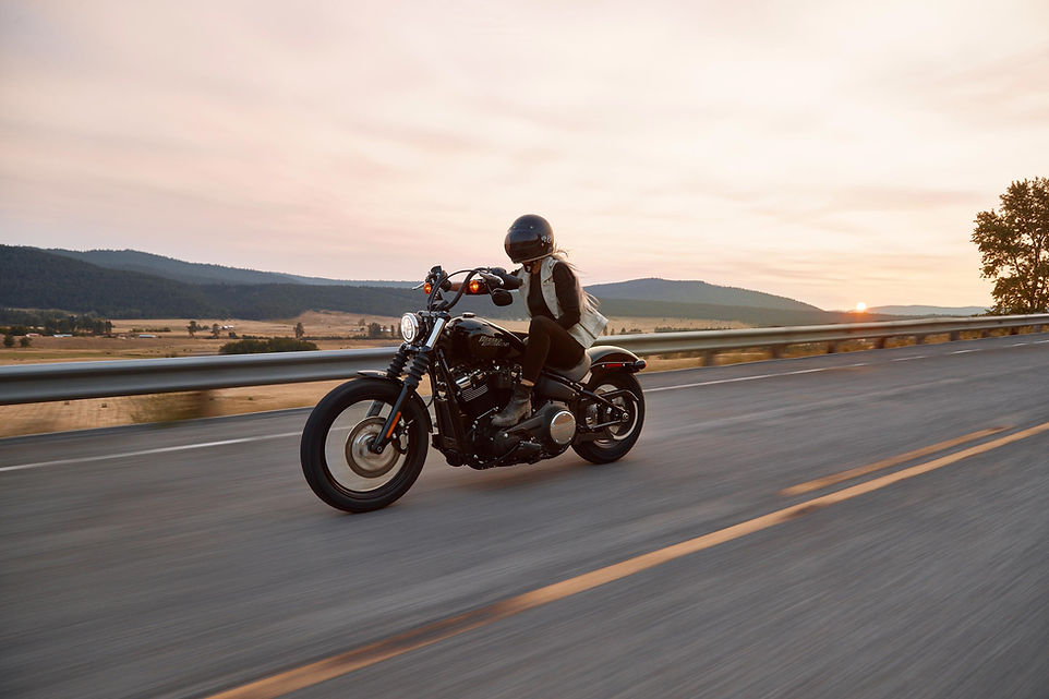 A woman rides a Harley-Davidson along a road.