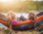 View from behind two girls sitting in a hammock together in the middle of a homeschool day.