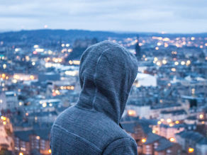 man with hood up looking over edinburgh city