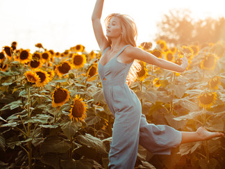 Frau mit weißem Hosenanzug tanzt in einem Sonnenblumenfeld