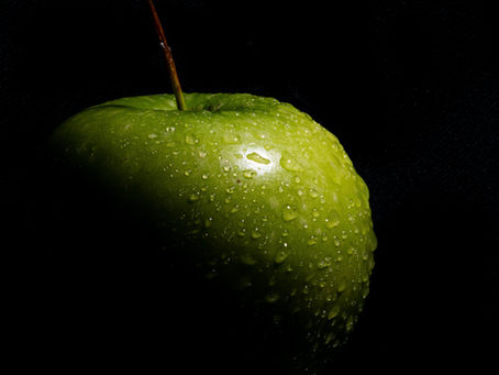 Close-up of a green apple covered in condensation and surrounded by darkness
