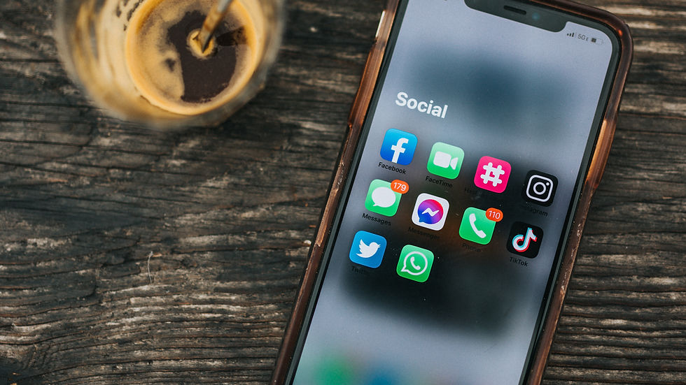 Smartphone with social apps open on screen, lies on wooden table. Nearby, a half-empty glass of coffee with a metal spoon. Cozy setting.