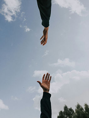 Two hands reaching out toward each other against a wide open sky, symbolising connection, support, and hope.