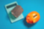 Orange piggy bank, wooden house, and mint calculator on blue background. Symbolizes savings and finance.