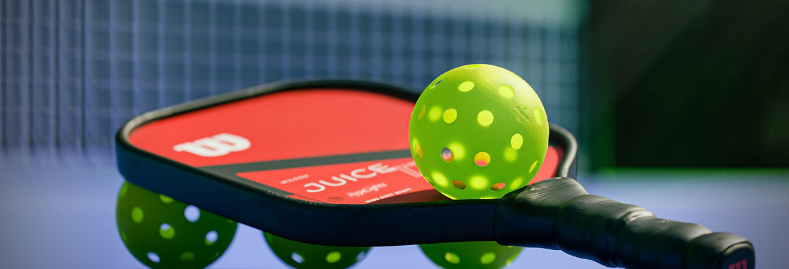 Pickleball-Schläger und gelber Ball liegen auf einem blauen Court
